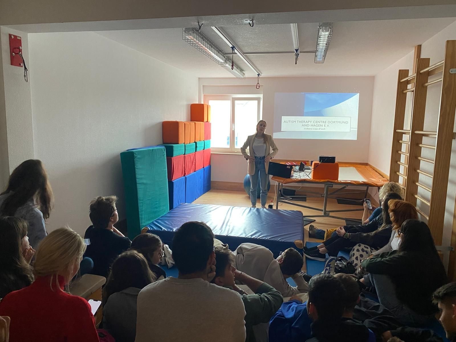 Trainerin hält eine Sitzung über das Autismus-Therapiezentrum Dortmund und Hagen vor sitzenden Teilnehmenden