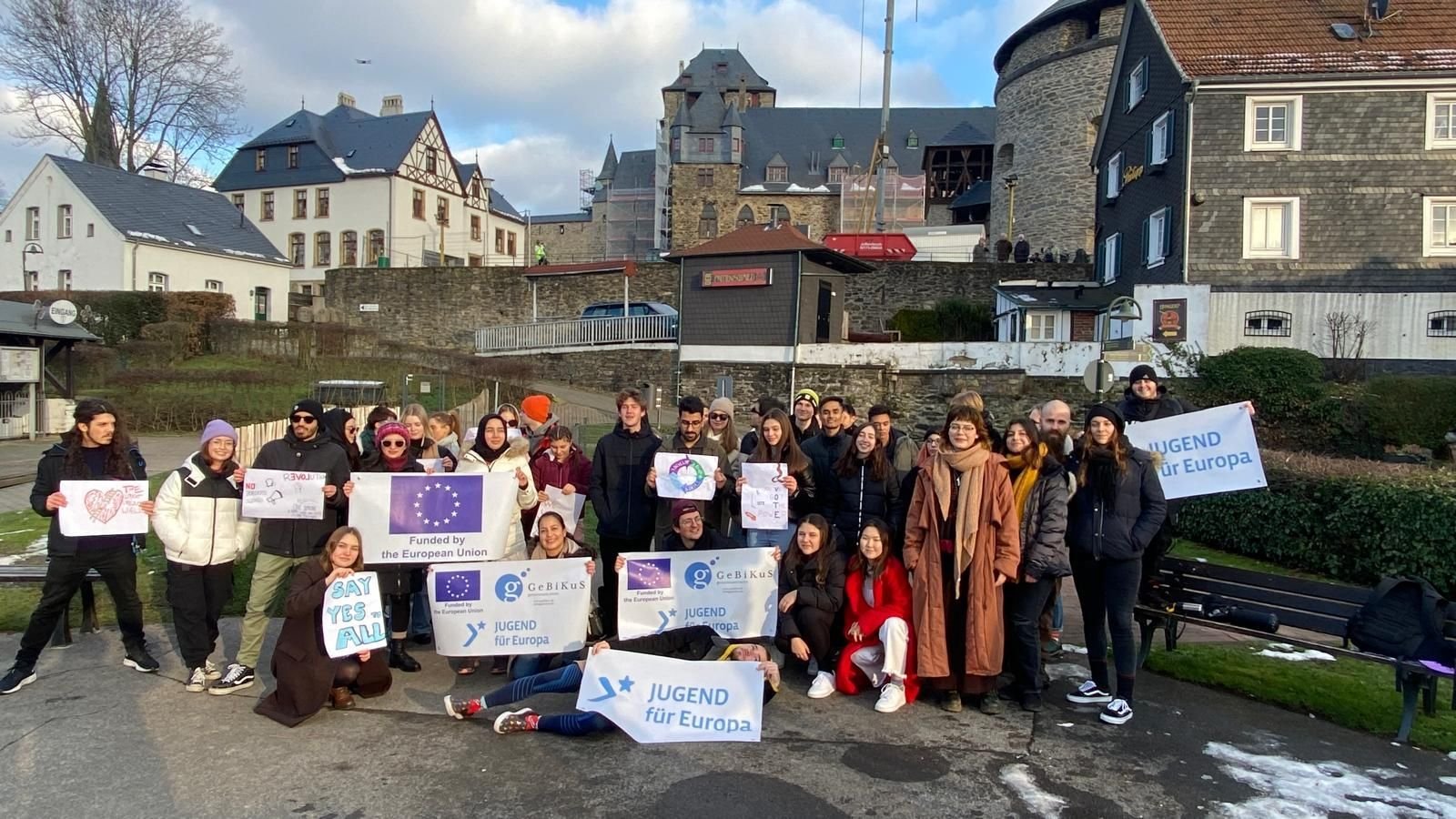 Gruppe von Jugendlichen mit „Say Yes to All“- und Erasmus+-Schildern vor einer Burgkulisse
